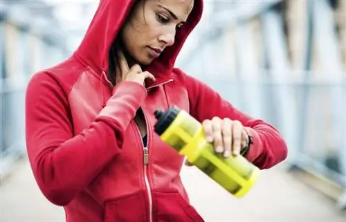 Женщина чувствует пульс на шее и держит в руке бутылку с водой