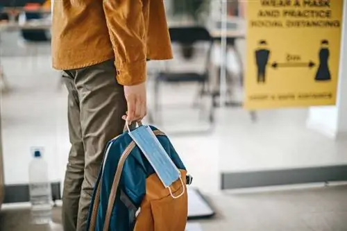 Мужчина стоит в аэропорту с маской и рюкзаком
