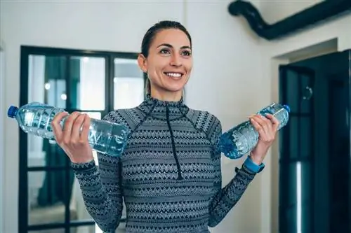 Женщина занимается спортом с бутылками с водой