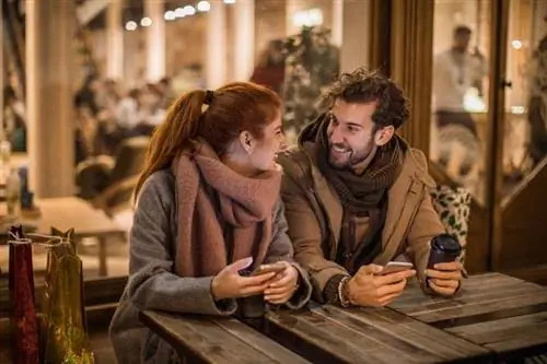 Мужчина и женщина сидят за столом снаружи со смартфоном в руке