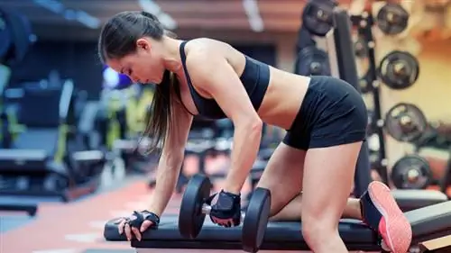 женщина в спортзале выполняет упражнения с гантелями