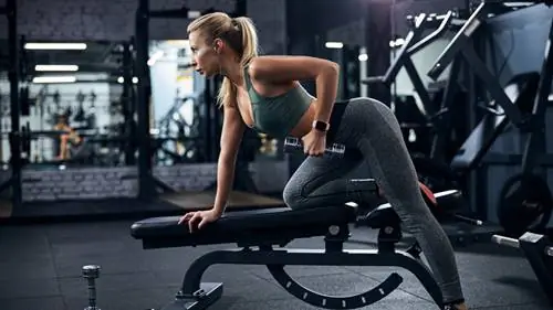 Женщина в спортзале гребет гантели