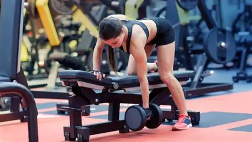 Женщина растягивает руку и плечо с гантелью