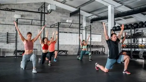 Группа людей разминается в тренажерном зале с выпадами и над головой