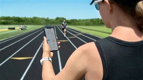 Тренер, стоящий на беговой дорожке, смотрит на приложение Garmin Clipboard на смартфоне, к нему бежит бегун на заднем плане. Тренер, стоящий на беговой дорожке, смотрит на приложение Garmin Clipboard на смартфоне, к нему бежит бегун на заднем плане.