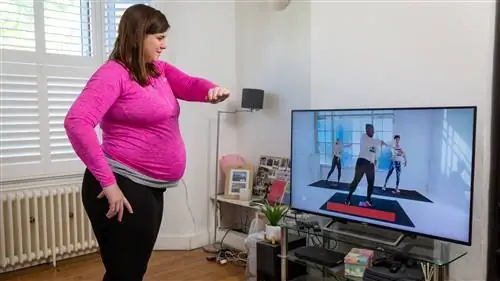 Женщина следит за тренировкой Couch to Fitness для беременных по телевизору Женщина следит за тренировкой Couch to Fitness для беременных по телевизору