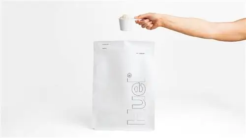Рука держит мерную ложку порошка-заменителя еды Huel Essential.