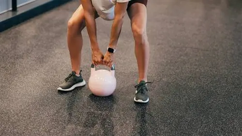 Крупный план нижней части тела женщины, которая собирается выполнить становую тягу с гирей