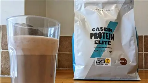 Myprotein Casein Protein Elite, смешанный в стакане с пакетом на заднем плане