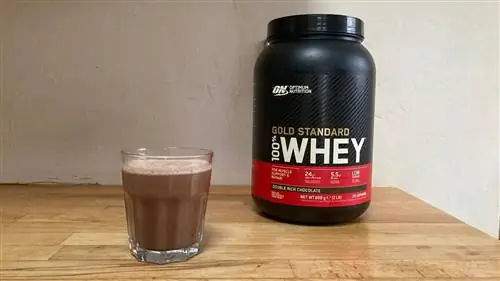 Баночка Optimum Nutrition Gold Standard 100% Whey с двойным шоколадным вкусом рядом с маленьким стаканчиком коричневого протеинового коктейля