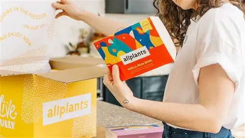 Женщина смотрит на этикетку на коробке от Allplants Женщина смотрит на этикетку на коробке от Allplants