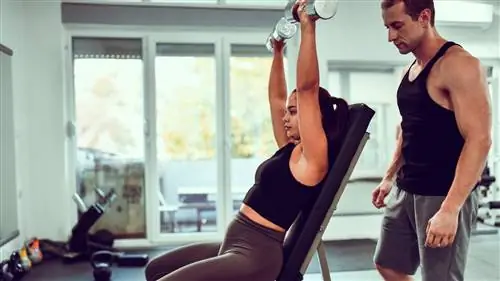 Женщина выполняет жим гантелей над головой сидя