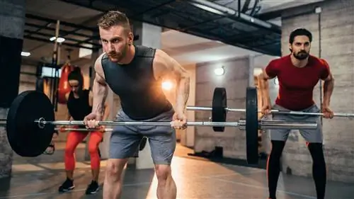 Двое мужчин и женщина выполняют тягу штанги в наклоне снизу в тренажерном зале.